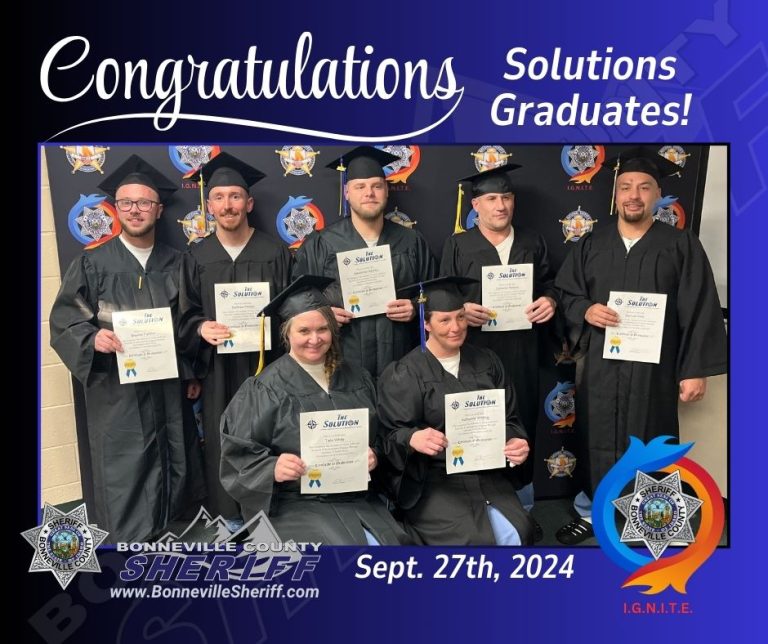 Seven adults in graduation gowns and caps hold certificates and smile at the camera in front of a Bonneville County Sheriff backdrop. The image says "Congratulations Solutions Graduates! Sept. 27th, 2024.