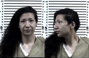 A woman wearing a tan prison uniform is shown in two mugshot photos: one facing forward and one in profile. A height chart is visible in the background.